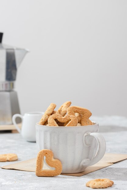 Foto biscotti a forma di cuore in una tazza bianca sfondo chiaro con una caffettiera