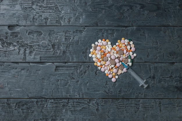 Heartshaped pills and a syringe on a wooden table