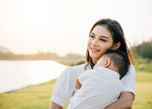 A heartwarming Mother's Day moment captured in the park at sunset. Beautiful mother cradles her sleeping baby, basking in peaceful nature and lovingly smiling at her newborn. Family care at its finest