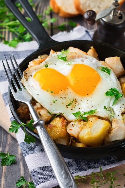 Hearty breakfast. Hash brown potatoes, chicken, onion, parsley, oregano and a fried egg in a frying pan on the old wooden table.