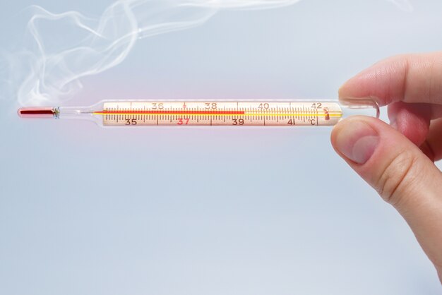 Heat mercury thermometer in the hand of a man isolated