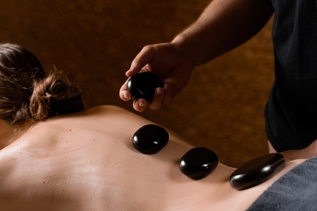 Heated stones on back of woman. Stone massage therapy in spa for relaxing.