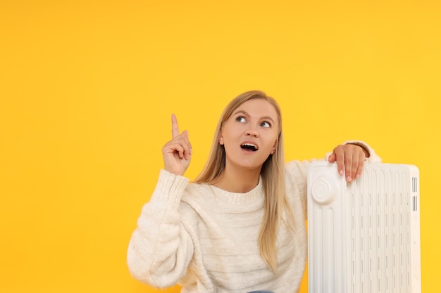 Heating season woman near heater on yellow background