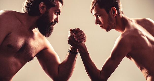 Heavily muscled bearded man arm wrestling a puny weak man Arms wrestling thin hand big strong arm in studio Two man's hands clasped arm wrestling strong and weak unequal match Arm wrestling