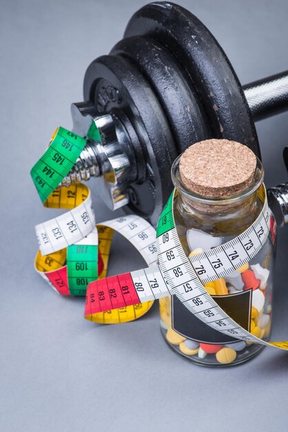 Heavy classical dumbbells with measuring tape and pills on grey