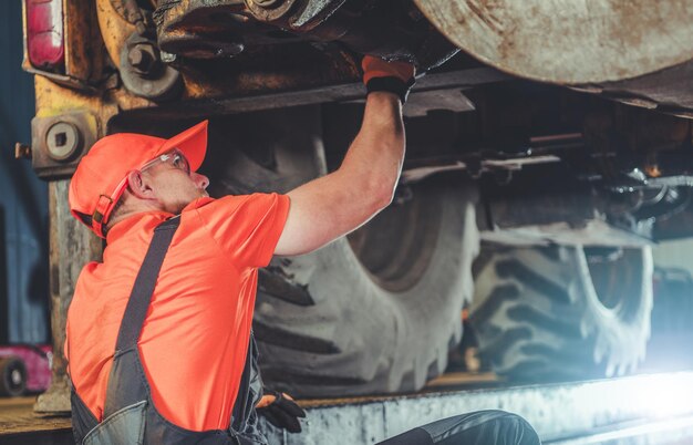 Photo heavy duty tractor under maintenance professional service worker caucasian industrial mechanic in his 30s