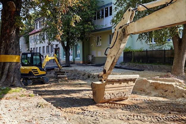 アスファルト道路が取り除かれた通りにある重い掘削機のバケツ 道路修理作業のための建設現場