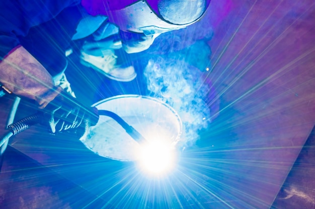 Heavy industry welder worker in protective mask hand holding arc welding torch working on metal construction