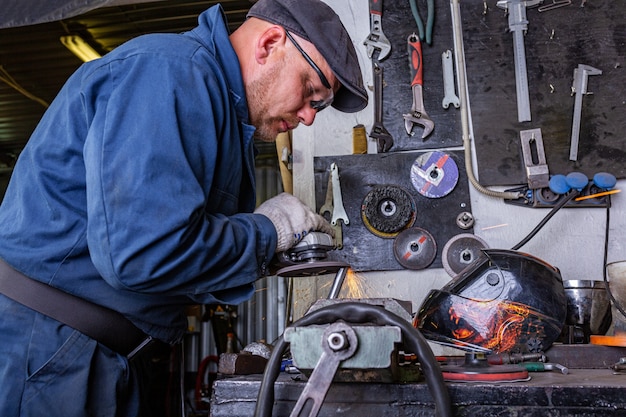 Heavy industry worker cutting steel with angle grinder at car service