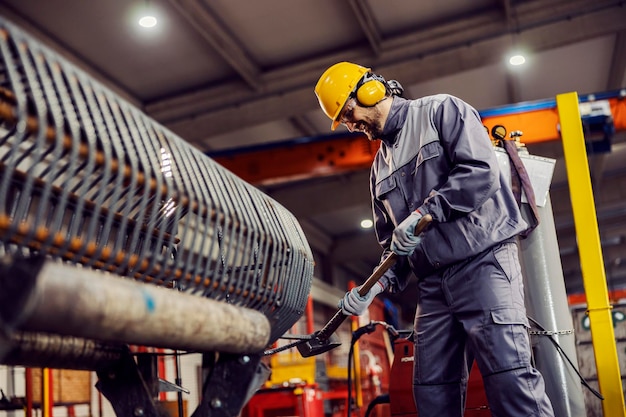 A heavy industry worker uses a hammer to fix metal work in the facility