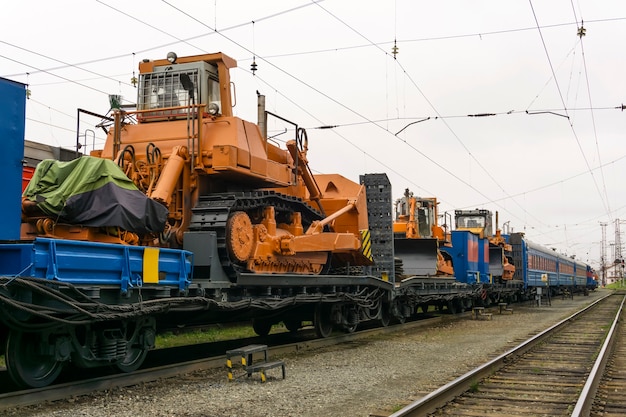 Тяжелые оранжевые бульдозеры стоят на платформе поезда для аварийно-восстановительных работ