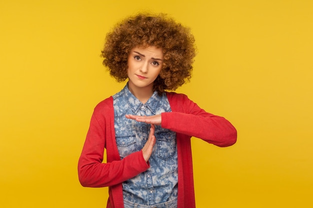 Heb alsjeblieft een pauze nodig Portret van een ongelukkige smekende vrouw met krullend haar die er moe uitziet en om een pauze vraagt met een time-out handgebaar waarschuwing voor deadline indoor studio shot geïsoleerd op gele achtergrond