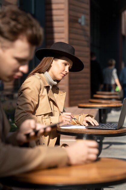 Hedendaagse jonge elegante zakenvrouw of student in slimme vrijetijdskleding die naar een laptopscherm kijkt terwijl ze buitenshuis netwerken