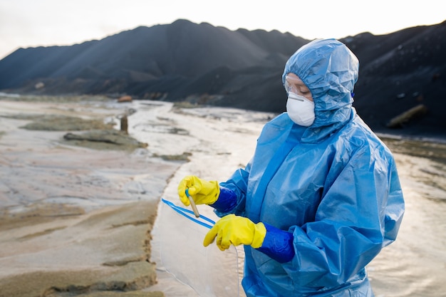 Hedendaagse onderzoeker of ecoloog die een kolf met een monster vuil water in het zakje stopt terwijl hij onderzoek doet naar vervuild gebied