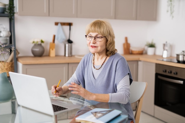 Hedendaagse volwassen vrouw die voor de laptop aan de keukentafel zit en met de leraar praat tijdens online les