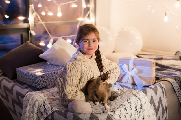 Heel mooi en charmant klein donkerharig meisje in witte trui heeft een levend konijn in het interieur van het huis. Nieuwjaar. Kerstmis. Haas. Studio.