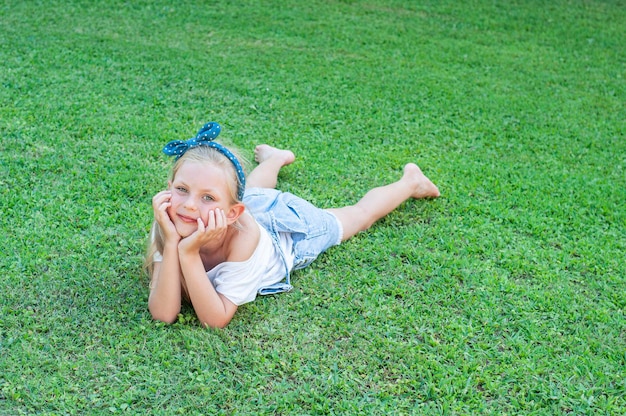 Ð¡heerful little girl in a denim jumpsuit, lying on a green grass