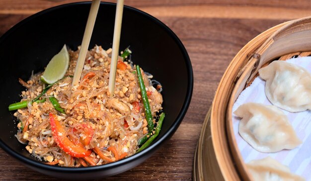 Heerlijk Aziatisch eten wok met noedels met eetstokjes knoedels in bamboe stoomboot op houten achtergrond Selectieve aandacht Aziatisch eten concept