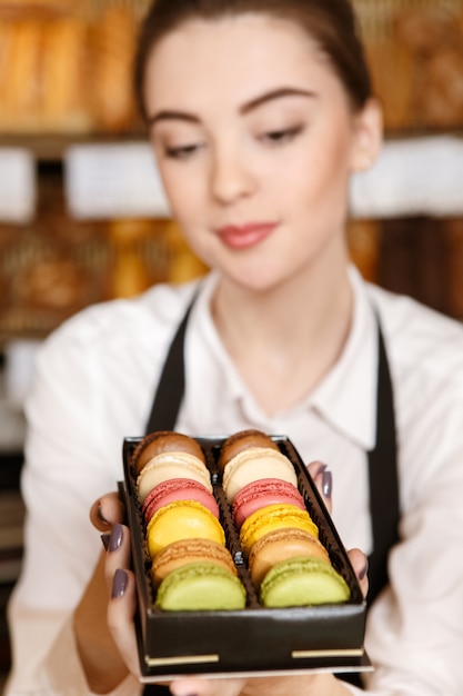 Heerlijk begin van de dag. Close-upportret van een mooie vrouwelijke bakker die de cake van het fruittaartje aan de showcase zet