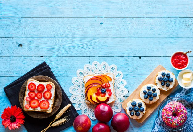 Heerlijk gezond ontbijt, fruitsandwiches met verschillende vullingen, kaas, banaan, aardbei, vissen, boter, bosbessen, op een andere houten achtergrond.