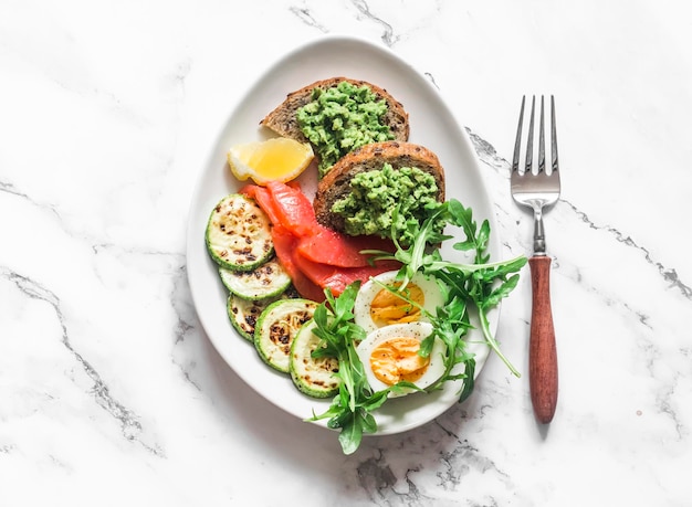 Heerlijk ontbijt gekookt ei gerookte zalm gegrilde courgette avocado sandwich op een licht marmeren achtergrond bovenaanzicht