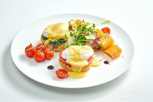 Heerlijk ontbijt met gepocheerde eiertoast en hollandaisesaus, licht gezouten zalm in een wit bord. Geïsoleerd op een witte ondergrond.
