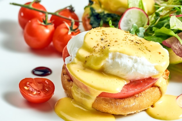 Heerlijk ontbijt met gepocheerde eiertoast en hollandaisesaus, licht gezouten zalm in een wit bord. Geïsoleerd op grijze ondergrond.