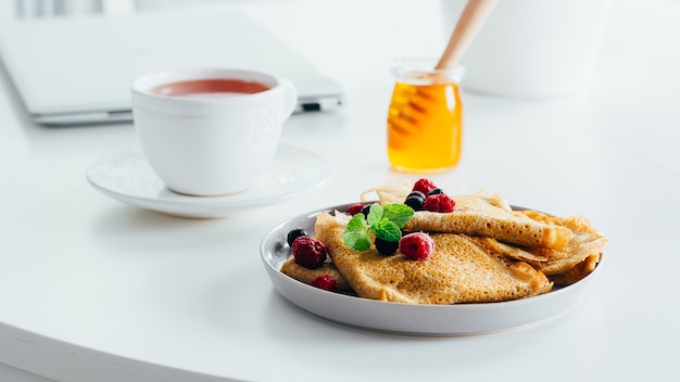 Heerlijk ontbijt. Witte bureaublad tafel met laptop en verse pannenkoeken pannenkoeken, kopje thee