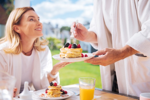 Heerlijk ontbijt. Zorgzame liefhebbende echtgenoot die heerlijke warme pannenkoeken en vers sinaasappelsap serveert als ontbijt