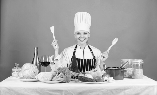 Heerlijk receptconcept Gastronomische hoofdgerechten Recepten Koken is haar hobby Gezonde voeding koken Meisje in hoed en schort Vrouw chef-kok die gezond voedsel kookt Verse groenten ingrediënten voor het koken van maaltijd
