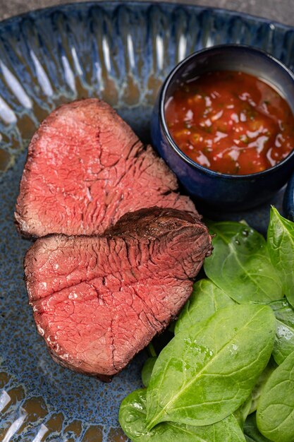 Foto heerlijk sappig gegrild stukje gegrilde steak met spinazie en sauzen op een glanzend blauw bord gesneden steak medium rare een stevige gourmet lunch restaurantvoorraad