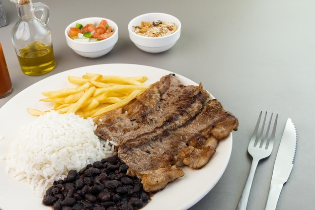 Heerlijk uitvoerend gerecht van biefstuk, rijst, bonen, friet en groene salade met sla, tomaat en ui vergezeld van farofa en vinaigrette Typisch Braziliaans eten Selectieve focus