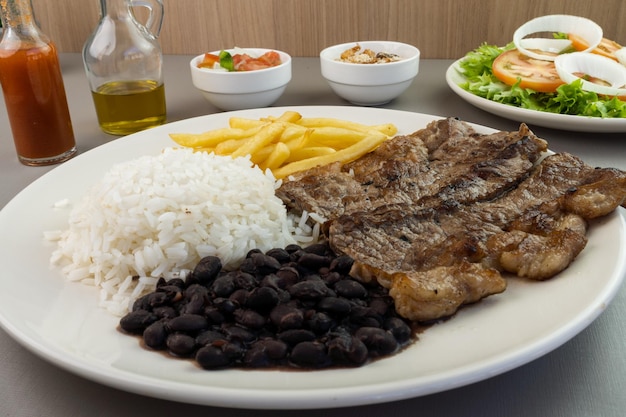 Heerlijk uitvoerend gerecht van biefstuk, rijst, bonen, friet en groene salade met sla, tomaat en ui vergezeld van farofa en vinaigrette typisch braziliaans eten selectieve focus