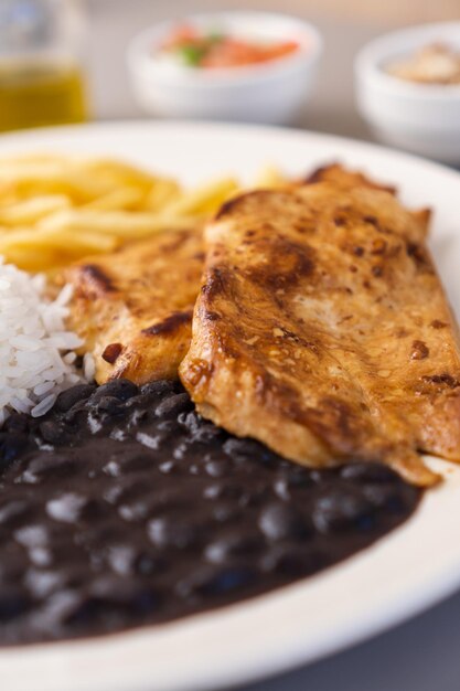 Heerlijk uitvoerend gerecht van kipfilet rijstbonen frietjes en groene salade met sla tomaat en ui vergezeld van farofa en vinaigrette Typisch Braziliaans eten Selectieve focus