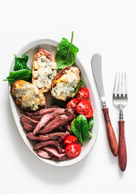 Heerlijk voorgerecht tapas lunch bord biefstuk groenten salade en geroosterde aardappelen met blauwe kaas op een lichte achtergrond bovenaanzicht