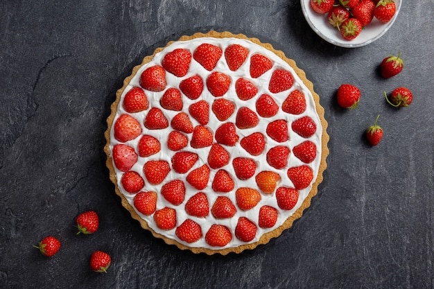 Heerlijke aardbeientaart met slagroom en mascarpone op een donkere betonnen ondergrond. bovenaanzicht.