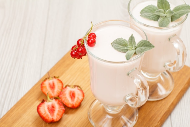 Heerlijke aardbeienyoghurt met muntblaadjes in glazen en vers gesneden aardbeien op houten snijplank