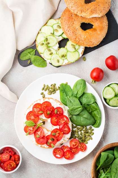 Heerlijke bagel gevuld met feta, tomaten en pompoenpitten en spinaziebladeren op een bord. Lichte gezonde vitaminesnack. Verticaal en bovenaanzicht