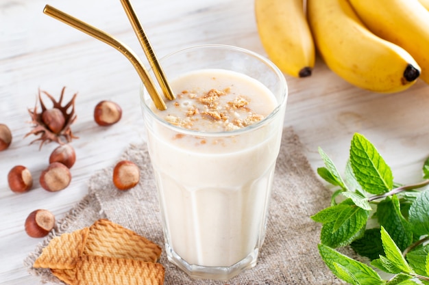 Heerlijke bananensmoothie met gesneden bananen en koekjes in glas op een witte achtergrond. gezond ontbijt.