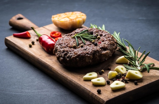 Heerlijke beef burger steak met specerijen en kruiden op snijplank en leisteen achtergrond