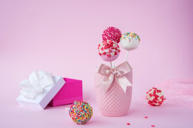 Heerlijke cake en een cadeau op een roze achtergrond, naast een rood en roze lint.