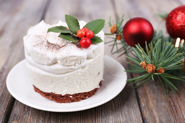 Heerlijke cake op schotel met hulst en bes op kerstversiering en houten achtergrond