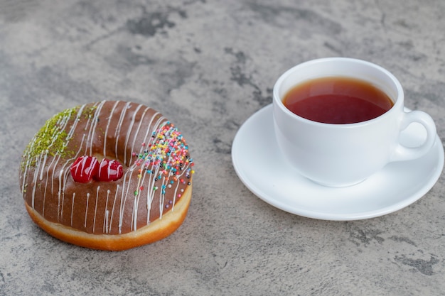 Heerlijke chocolade geglazuurde donut en kopje thee op stenen achtergrond.