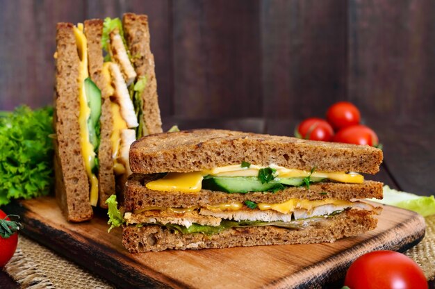 Heerlijke club sandwich met roggebrood, kip, kaas, komkommers, Groenen op een donkere houten achtergrond.