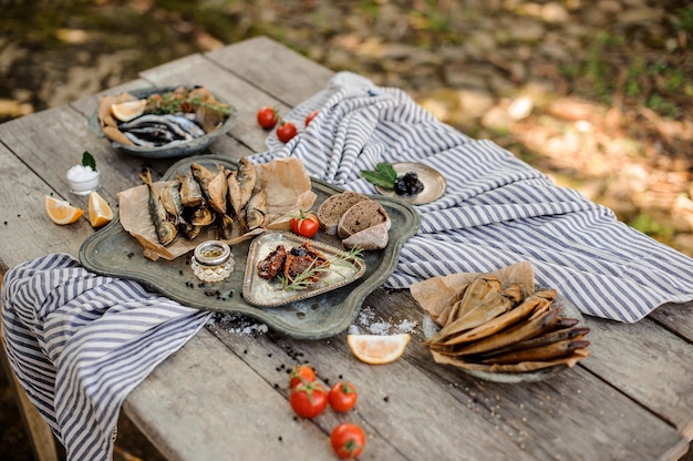 Heerlijke compositie op de houten tafel van de rookgedroogde horsmakreel en ansjovis met tomaten, rozemarijn, citroen, brood en andere smakelijke producten op het gestreepte servet buiten.