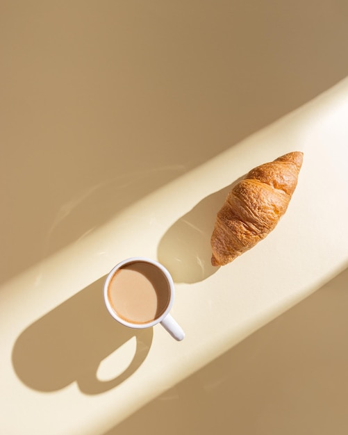 Heerlijke croissant en kopje koffie met melk op beige achtergrond met kopieerruimte