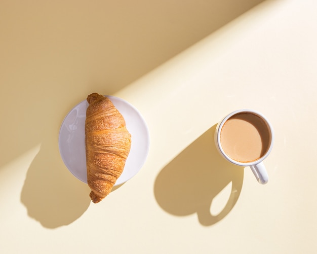 Heerlijke croissant en kopje koffie met melk op beige achtergrond