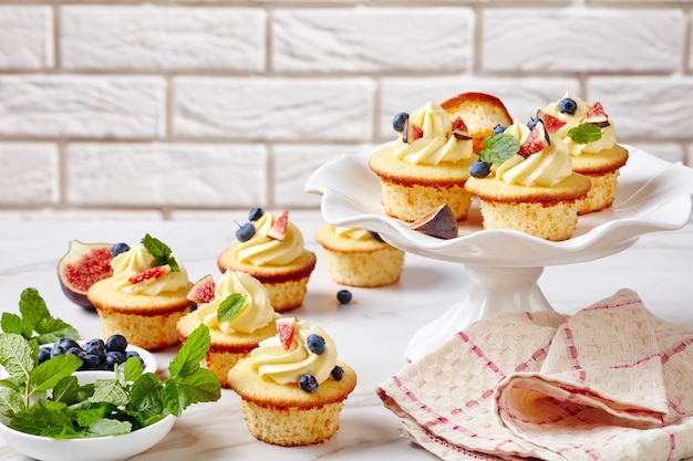 Heerlijke cupcakes met vanille clotted cream versierd met verse vijgen en bosbessen op een taart staan op een marmeren tafel, landschapsmening van bovenaf, close-up