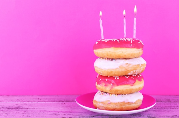 Heerlijke donuts met suikerglazuur en birthday kaarsen op tafel op lichte muur