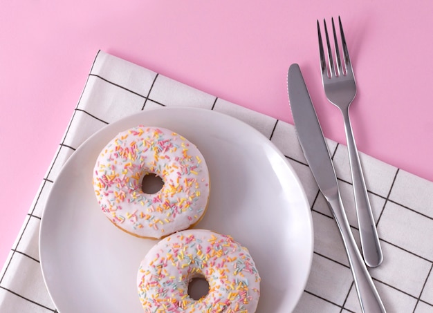 Heerlijke donuts op de plaat met servet en bestek op roze